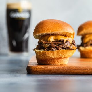 Side view of a Guinness braised beef slider on a wooden board with a glass of Guinness in the background.