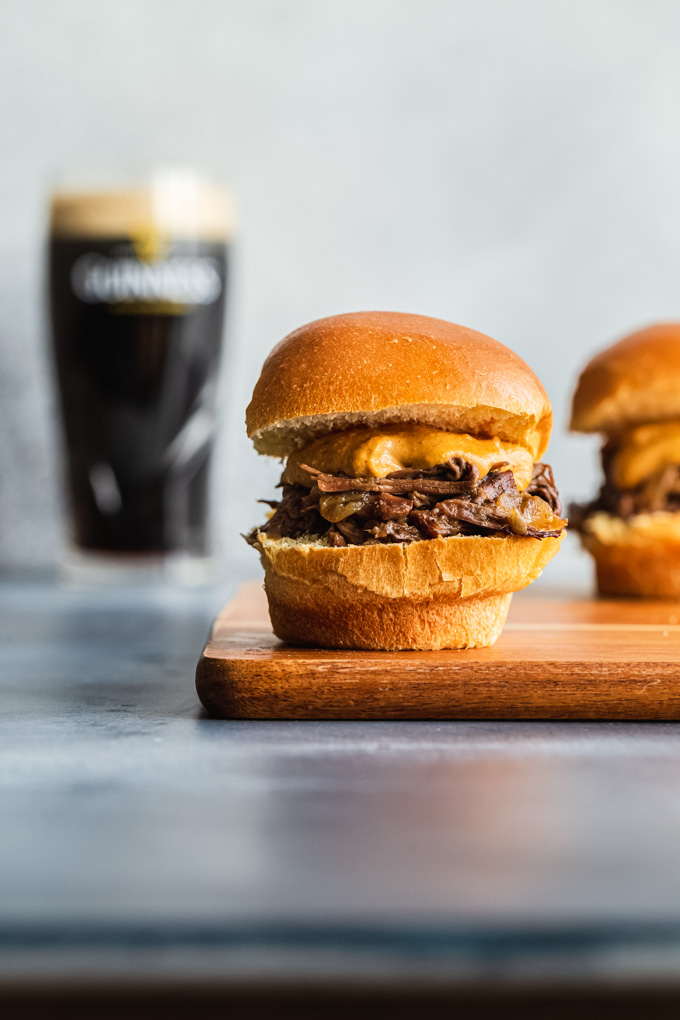 Side view of a Guinness beef slider on a cutting board with a glass of Guinness in the background.