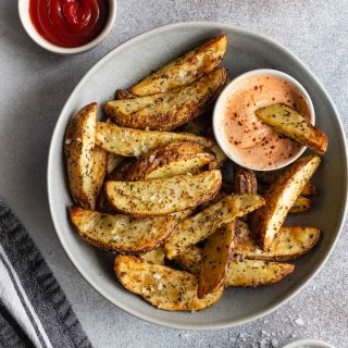 Overhead view of air fryer potato wedges in a grey bowl with dipping sauces off to the sides.
