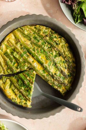 Overhead view of asparagus crustless quiche in a dish with a piece being removed.