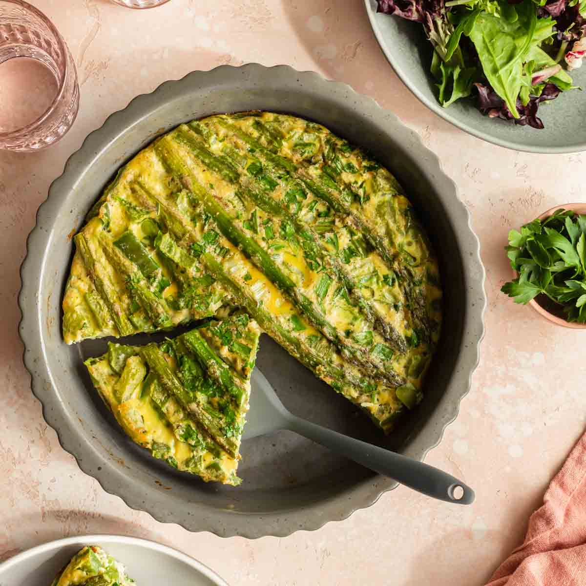 Overhead view of asparagus crustless quiche in a dish with a piece being removed.