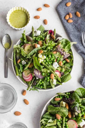 Overhead view of a spring salad on a plate with another salad and vinaigrette off to the sides.