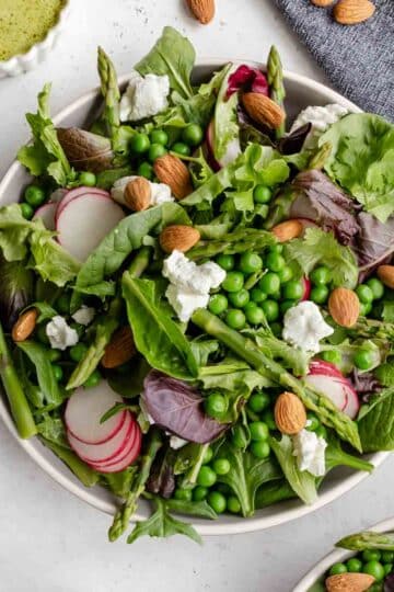 Overhead of asparagus and pea salad served on a plate with dressing on the side.
