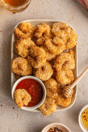 Overhead view of air fryer breaded shrimp on a plate with seafood sauce and a wooden honey dipper.