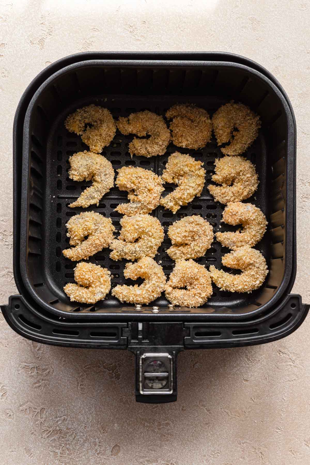 Overhead view of raw breaded shrimp in an air fryer basket.