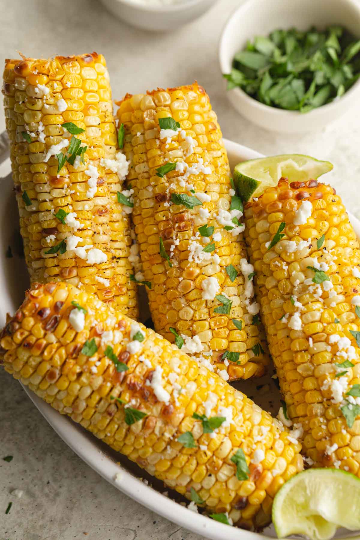 Corn on the cob in a white dish and topped with parsley and feta.