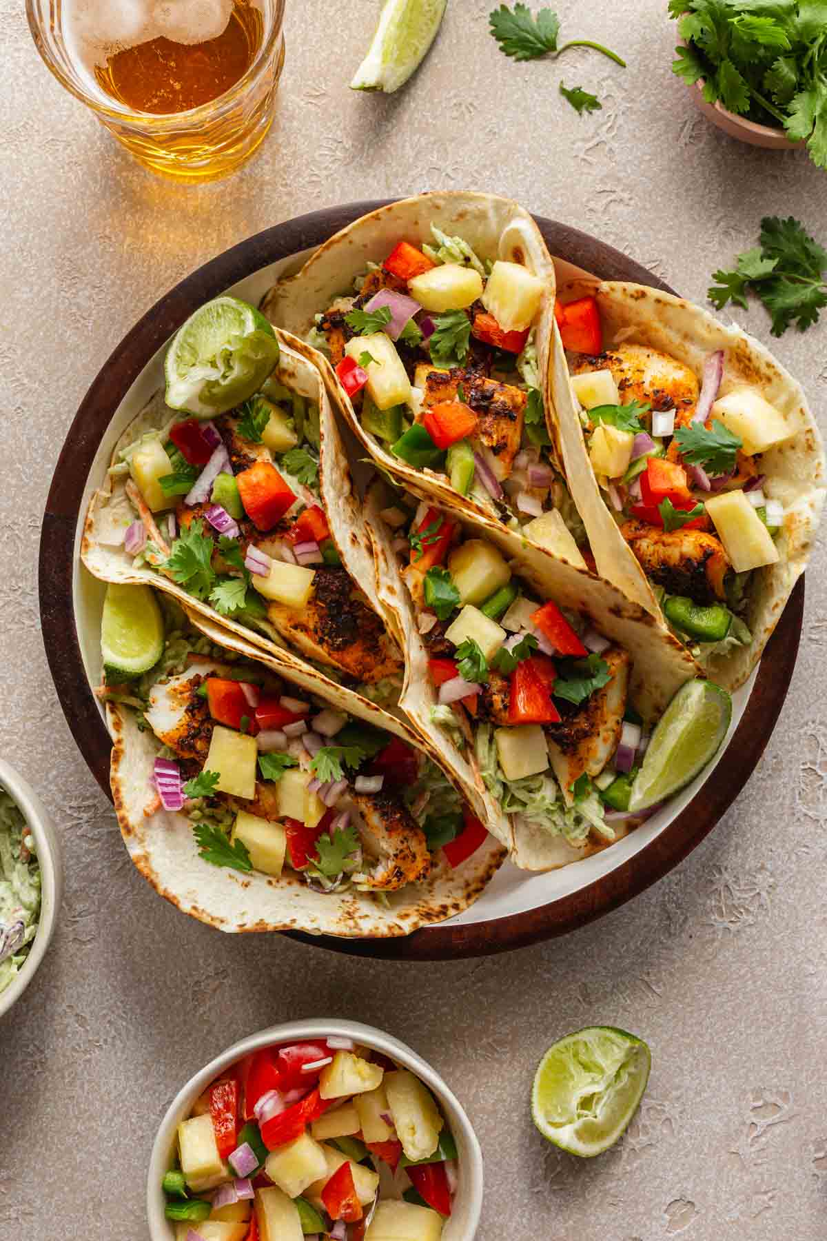 Fish tacos topped with pineapple salsa and arranged in a round serving dish.
