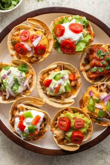 Overhead view of taco cups arranged on a round plate with a variety of toppings.