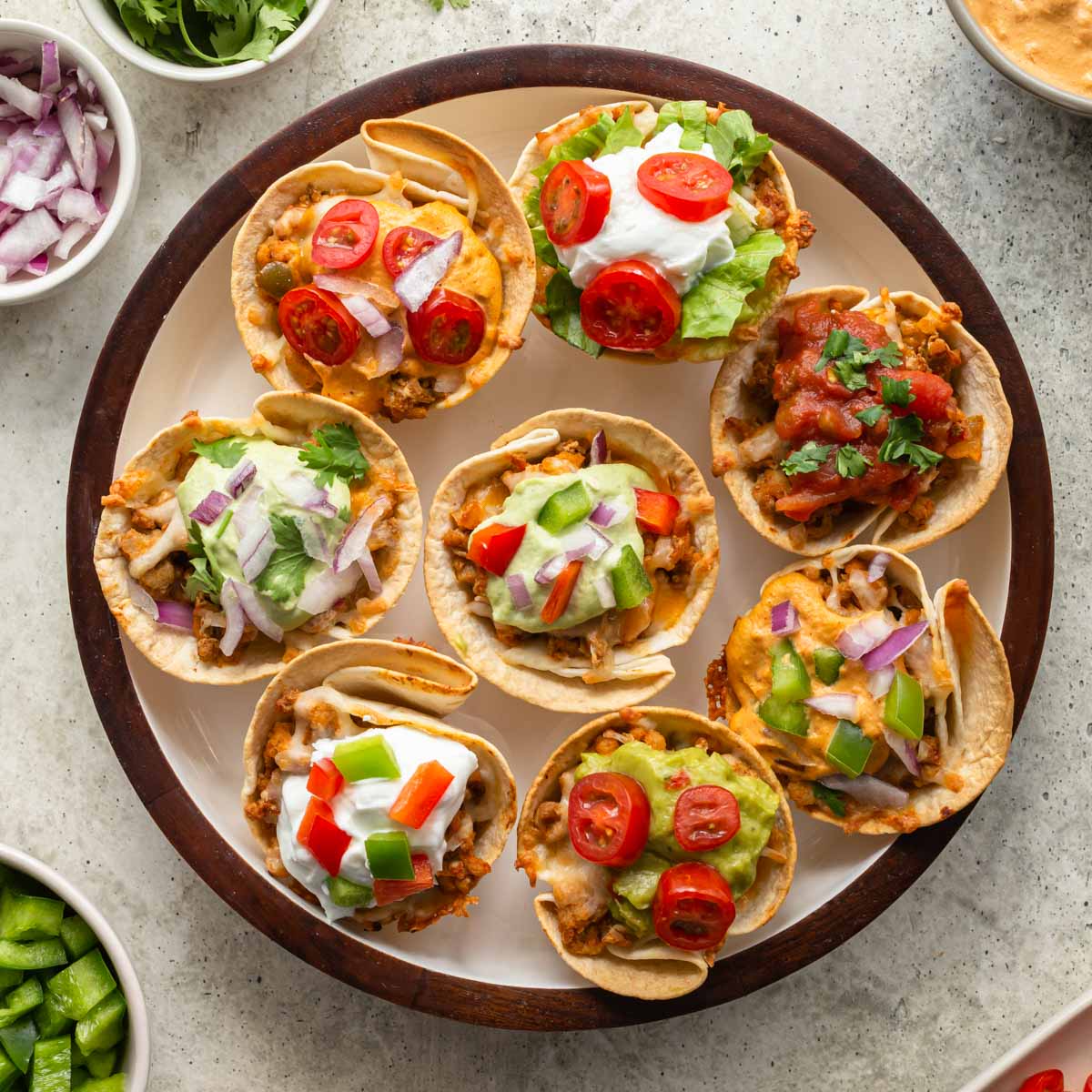 Overhead view of taco cups arranged on a round plate with a variety of toppings.