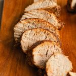 Close up side view of slices of pork tenderloin on a wooden board.