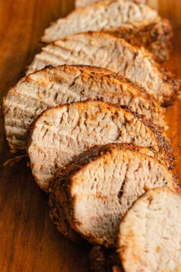 Close up side view of slices of pork tenderloin on a wooden board.
