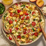 Grilled summer vegetable orzo salad served in a large bowl with serving spoons inserted into it.