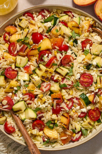 Grilled summer vegetable orzo salad served in a large bowl with serving spoons inserted into it.