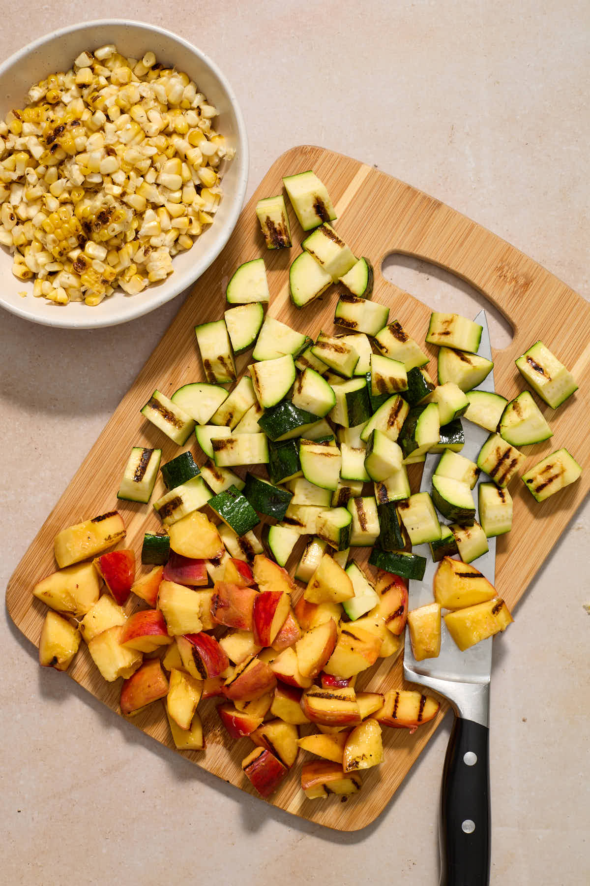 Chopped zucchini and peaches on a wooden board with a bowl of corn on the side.