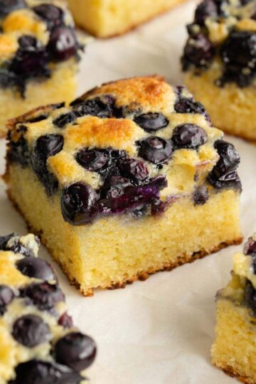 Blueberry cake cut into squares and arranged on parchment paper.