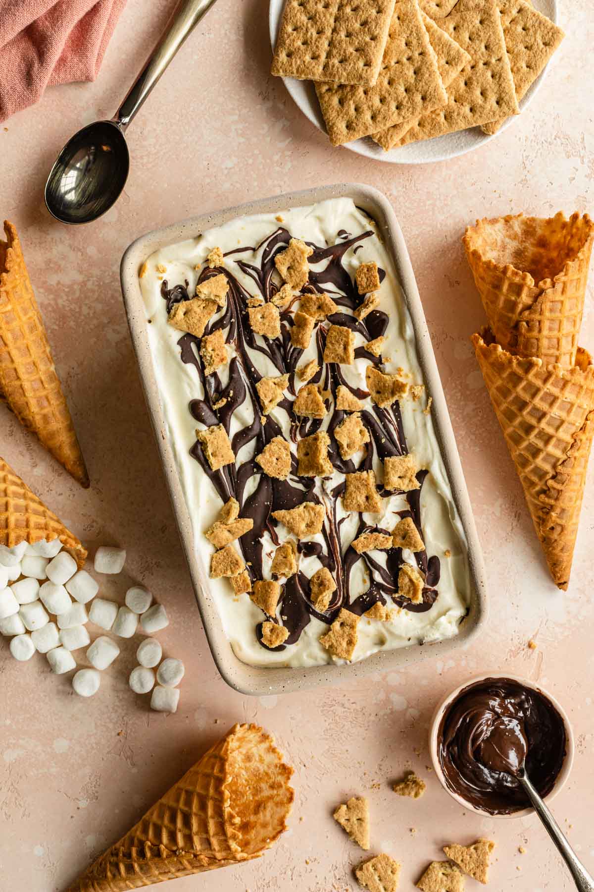 S'mores ice cream in a loaf pan and surrounded by marshmallows and waffle cones.