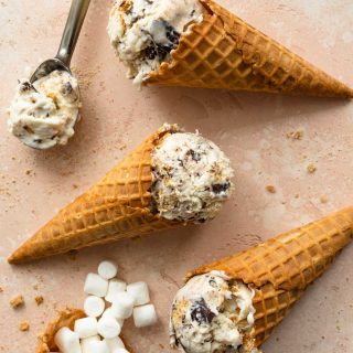 Three waffle cones filled with s'mores ice cream and arranged flat on a pink surface.