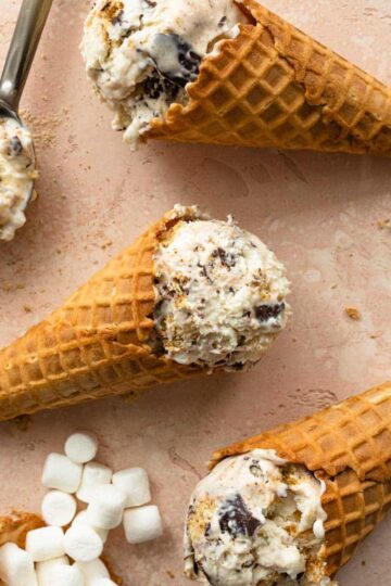 Three waffle cones filled with s'mores ice cream and arranged flat on a pink surface.
