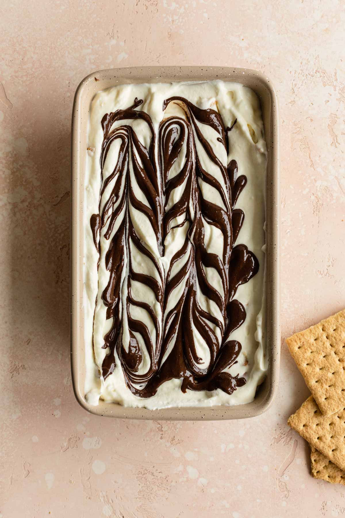 Ice cream mixture in a loaf pan with melted chocolate swirled around on the top.