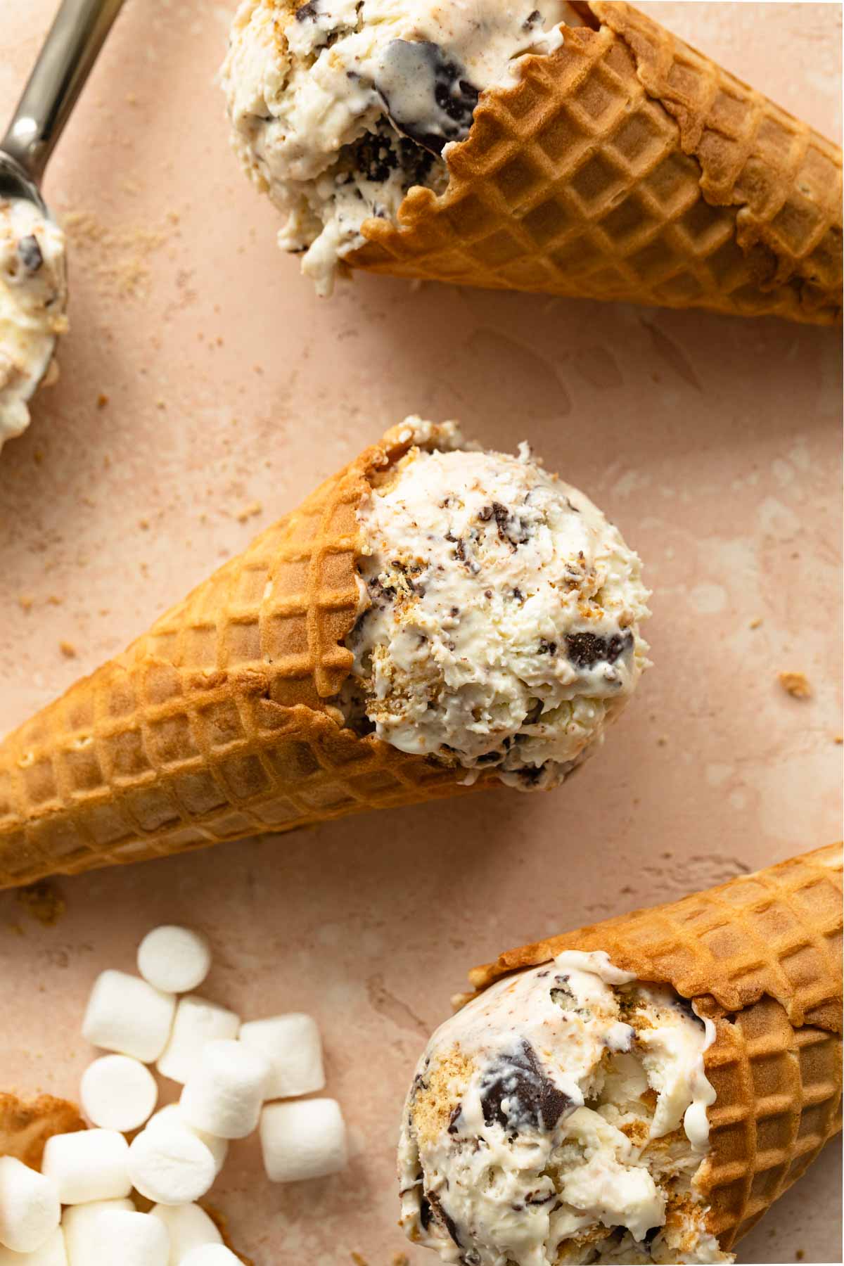 Close up of s'mores ice cream in waffle cones laying flat on a pink surface.