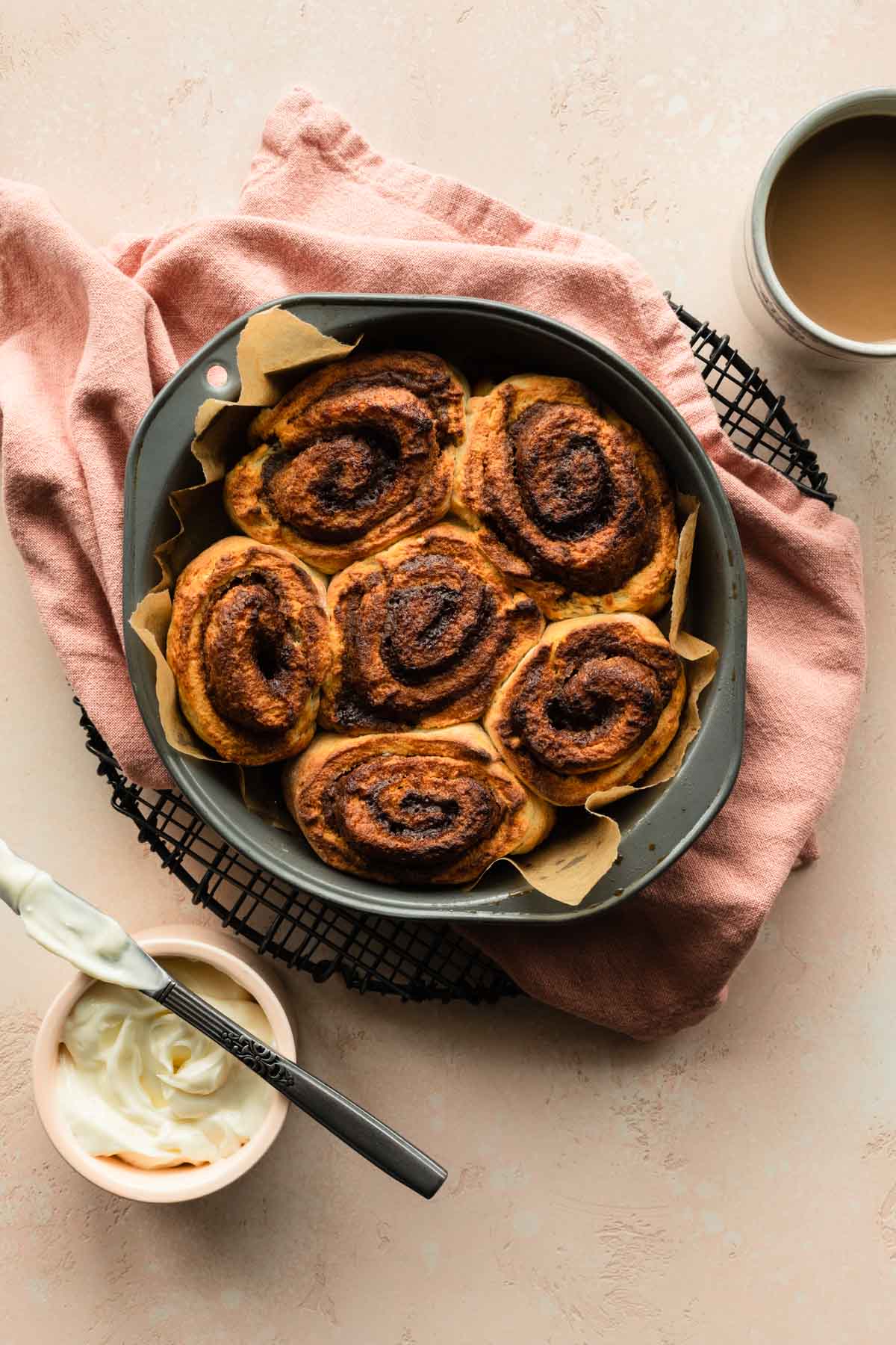 Overhead of air fryer cinnamon rolls in a round cake pan on a cooling rack.