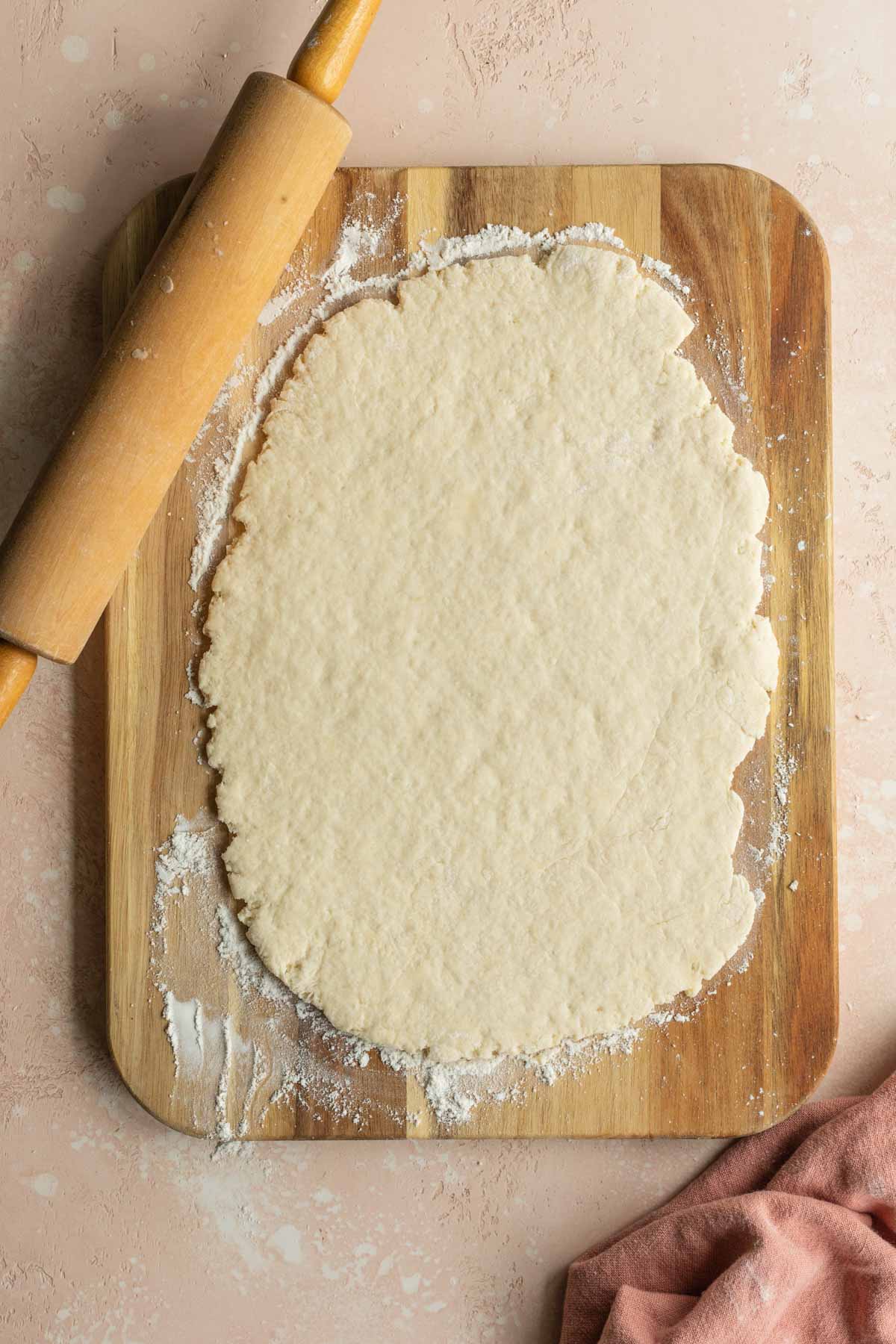 Rolled out dough on a wooden board next to a rolling pin.
