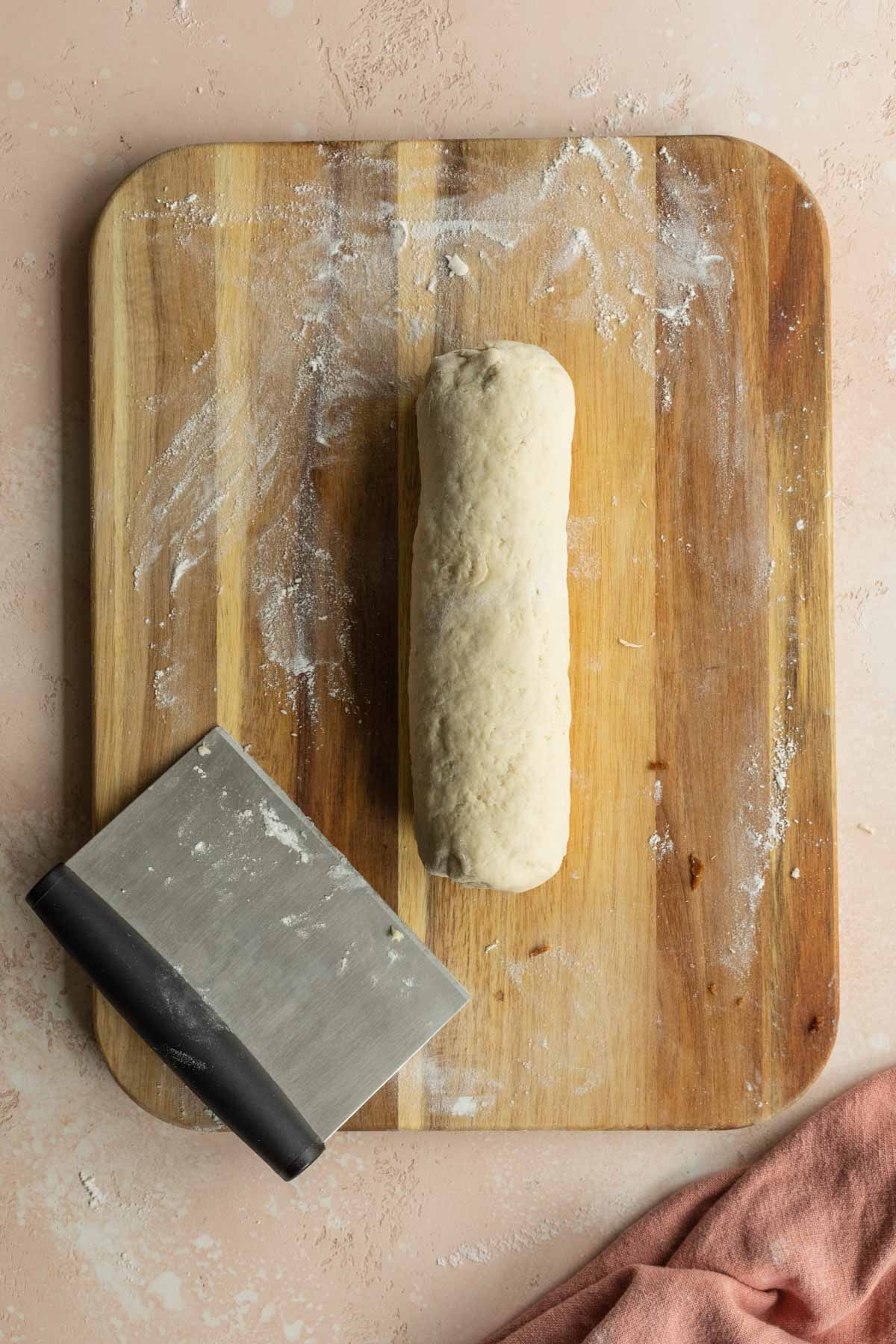 Cinnamon bun dough rolled into a log on a wooden cutting board.
