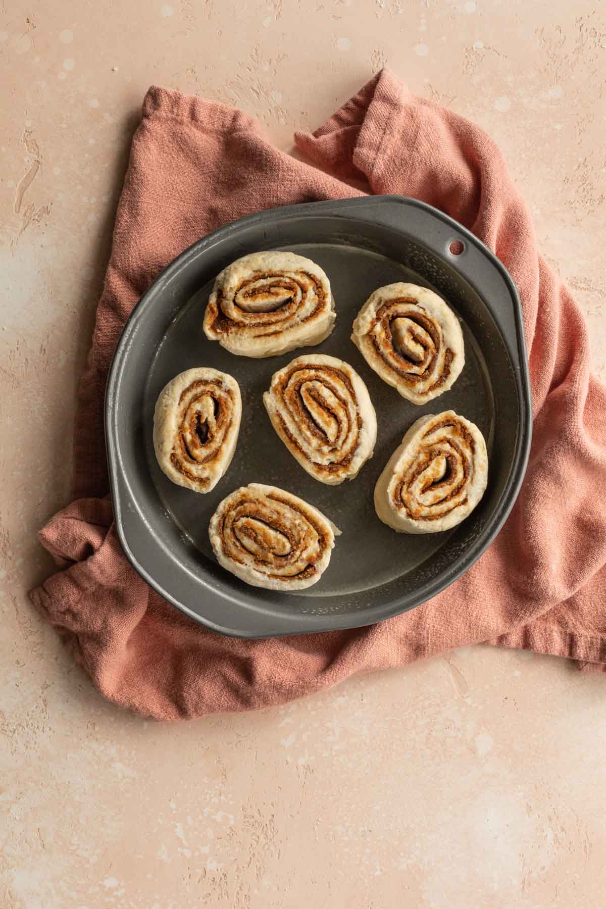 Pre-baked cinnamon rolls arranged in a round cake pan.