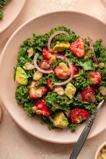 Strawberry kale salad on a pink plate.