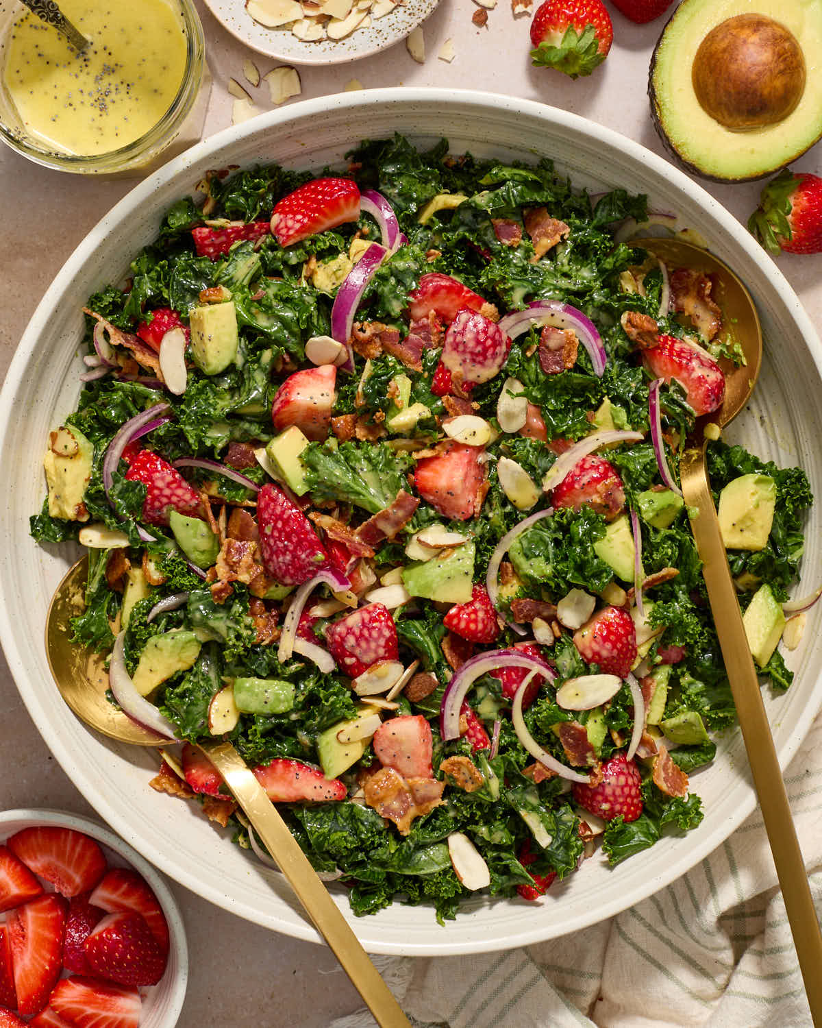 Salad in a large white serving bowl and gold salad tongs inserted into the salad.