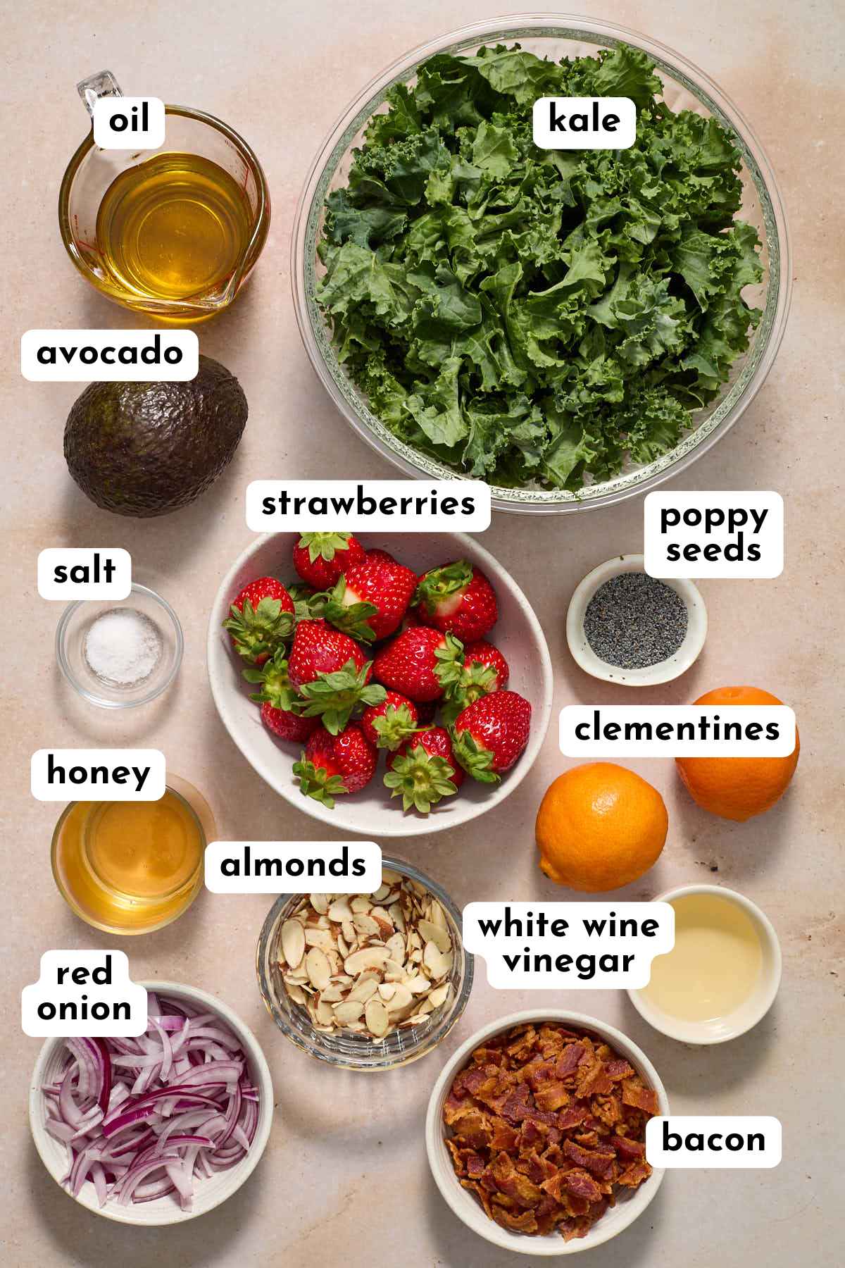 Ingredients to make a strawberry kale salad and poppy seed dressing arranged individually and labeled.