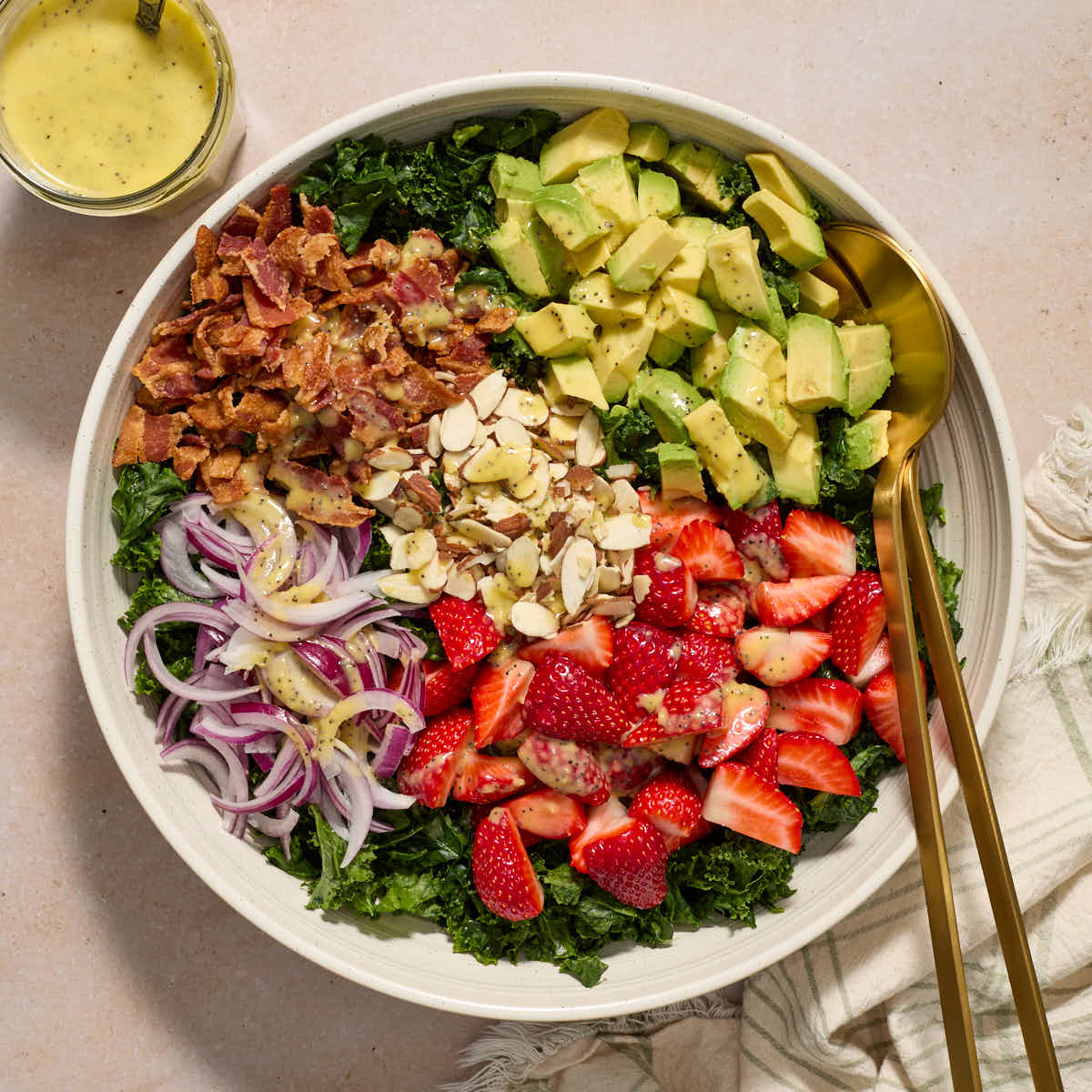 Salad ingredients added to a large white bowl in sections with a jar of dressing on the side.
