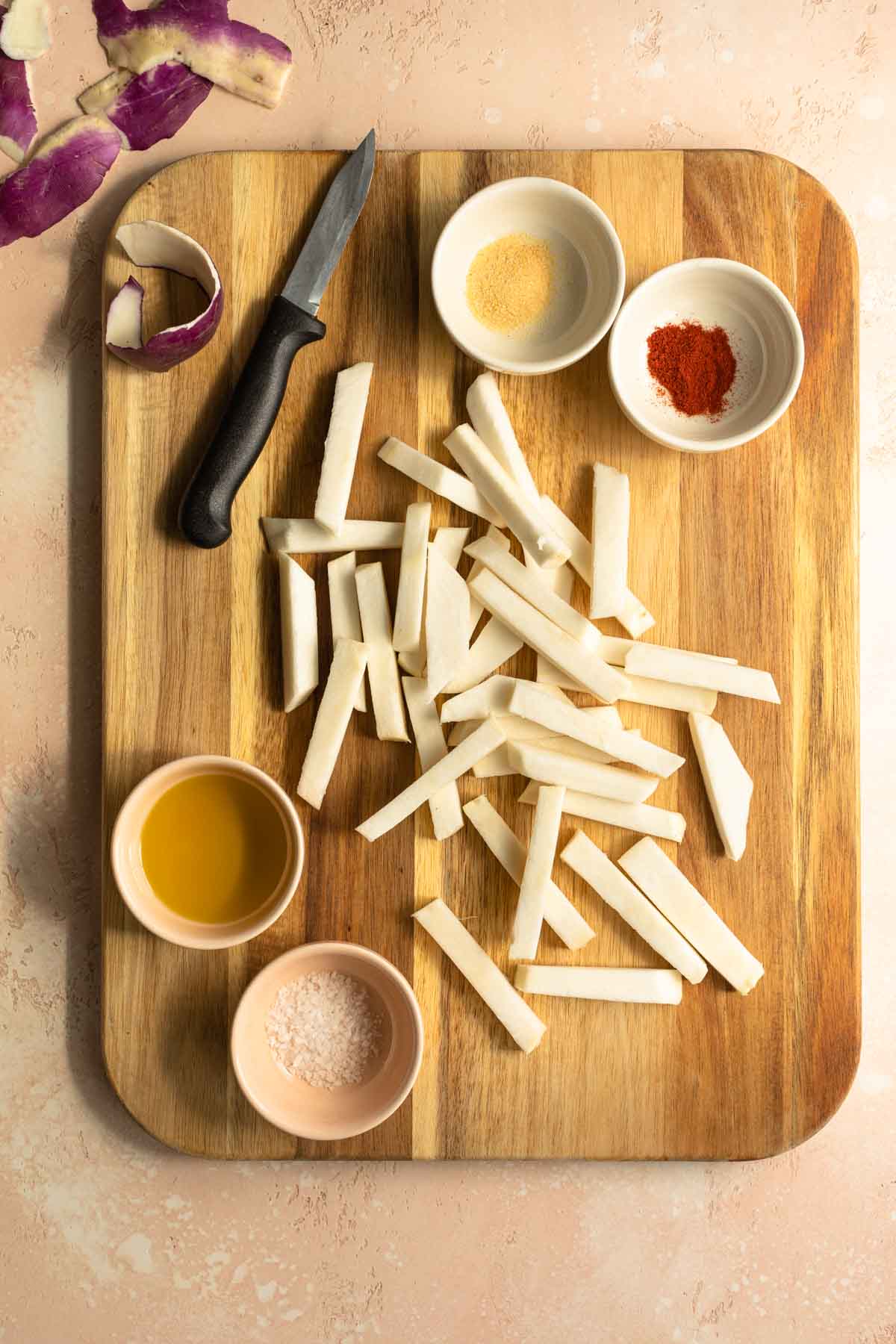 Raw turnip fries on a wooden cutting board with dishes of oil and seasonings on the side.