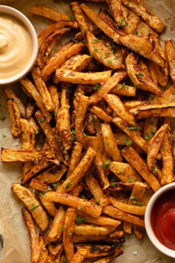 Overhead view of air fryer turnip fries arranged on a tray with ketchup and chipotle dip.