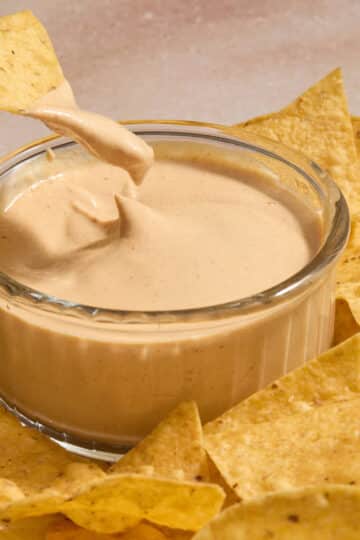 Dairy-free chipotle sauce in a small glass bowl with a chip being dipped into it.