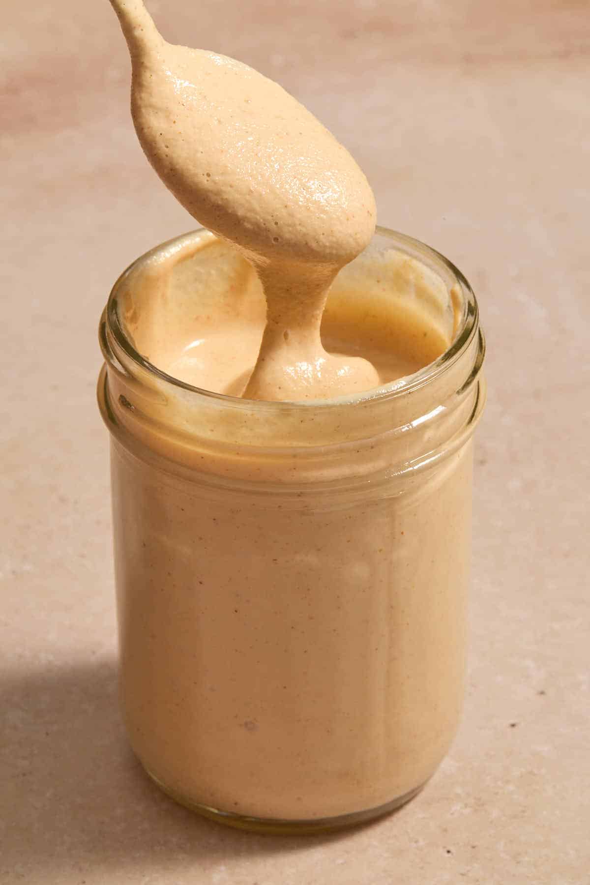 A spoonful of chipotle sauce being lifted out of a glass gar.