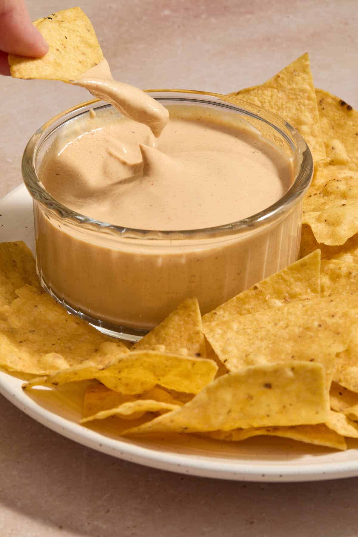 Chipotle sauce in a small bowl with chips on a plate and a chip being dipped into the sauce.
