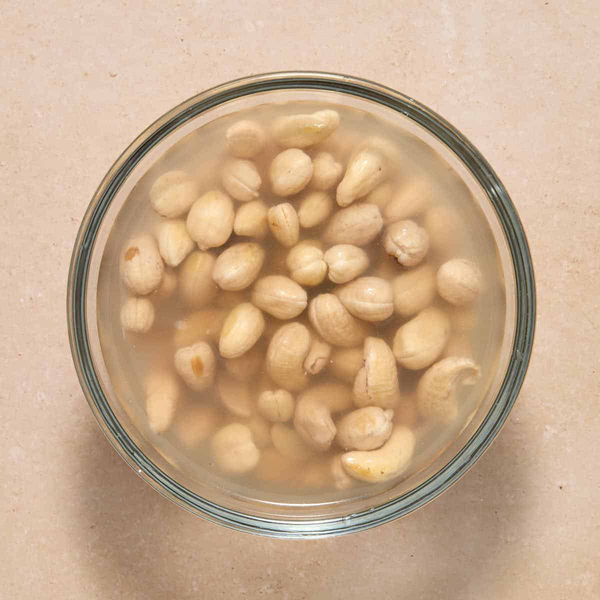 Cashews soaking in water in a glass bowl.