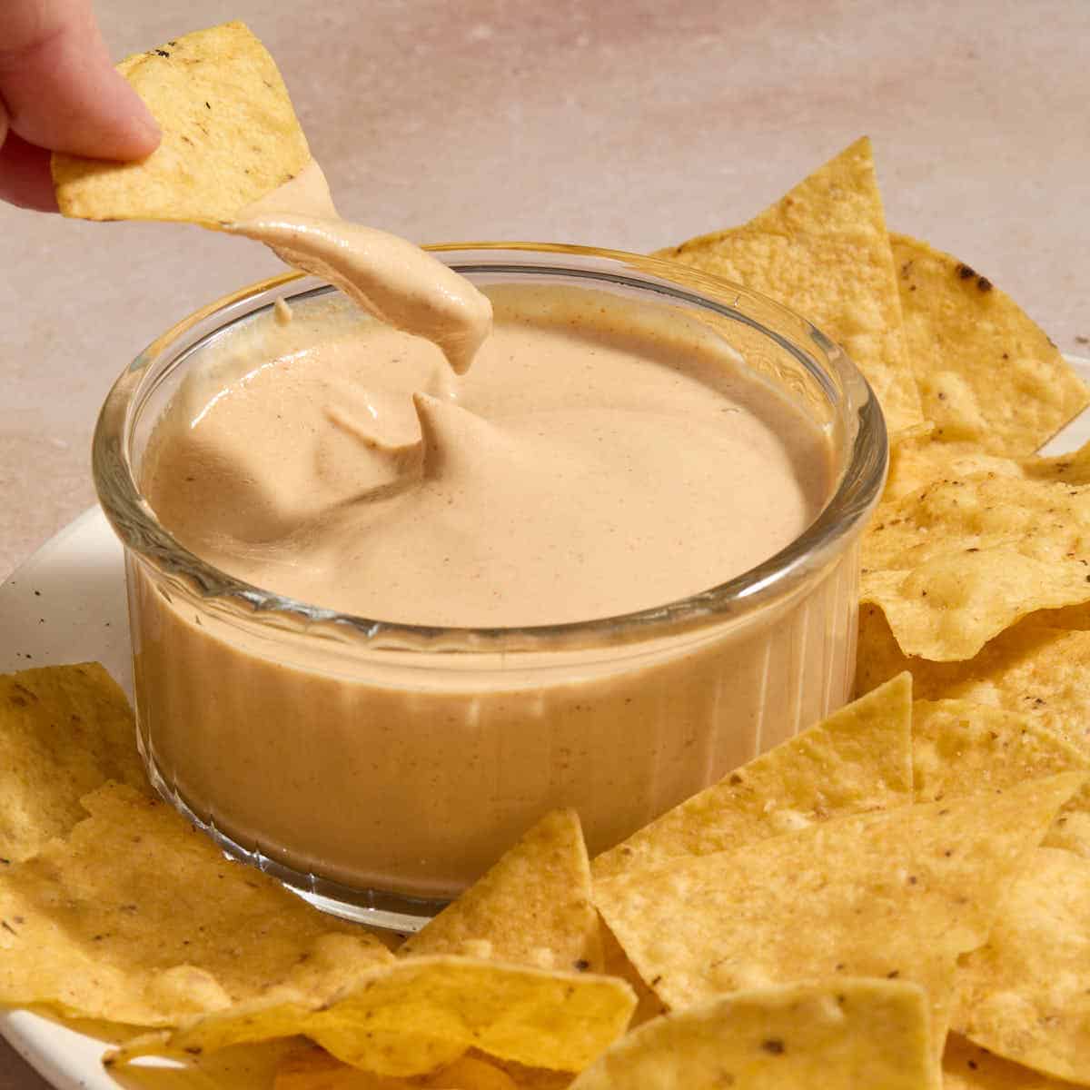 Dairy-free chipotle sauce in a small glass bowl with a chip being dipped into it.