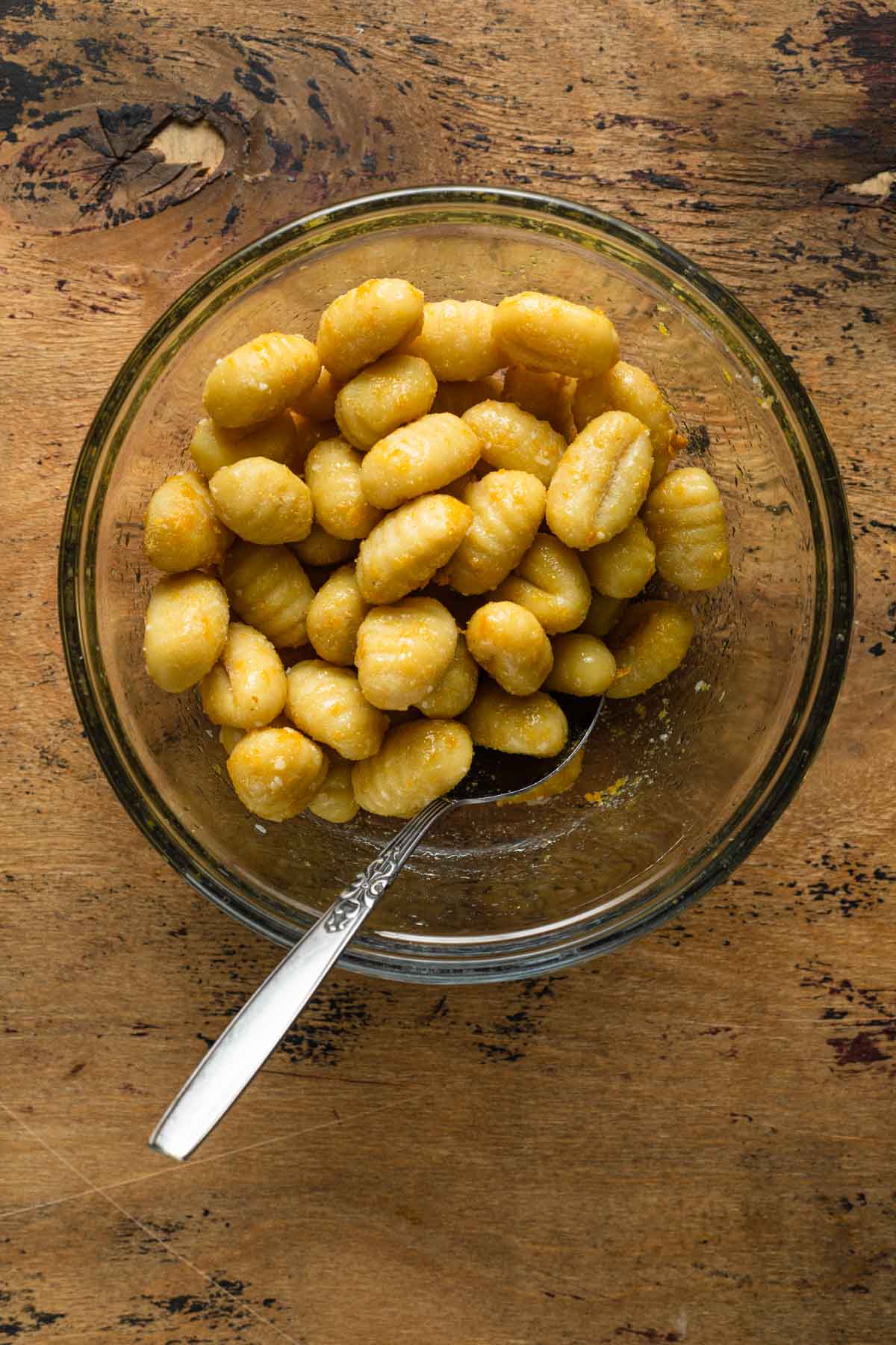 Seasoned gnocchi in a glass bowl with a spoon.