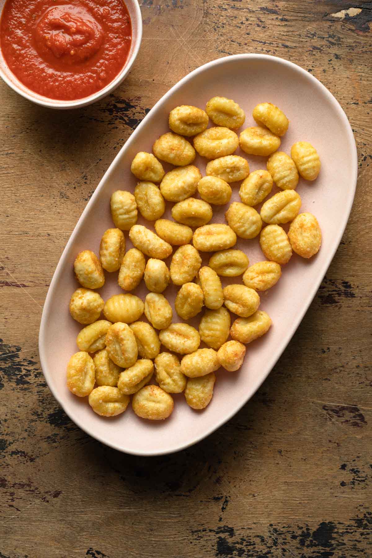 Crispy gnocchi served on a pink platter next to a small bowl of marinara sauce.