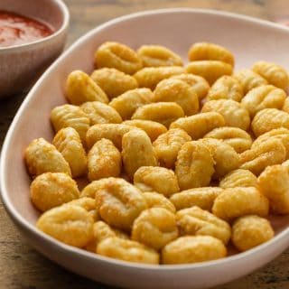 Close up view of air fryer gnocchi in a serving dish next to a bowl of marinara sauce.