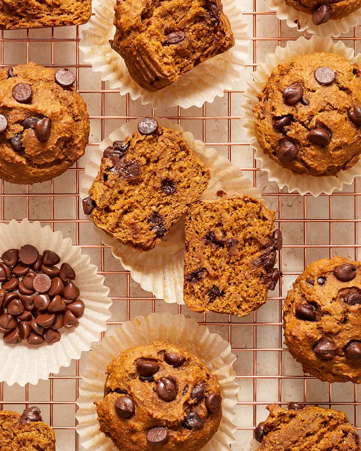 Overhead view of banana pumpkin muffins on a wire rack with one cut in half to expose the melted chocolate chips.