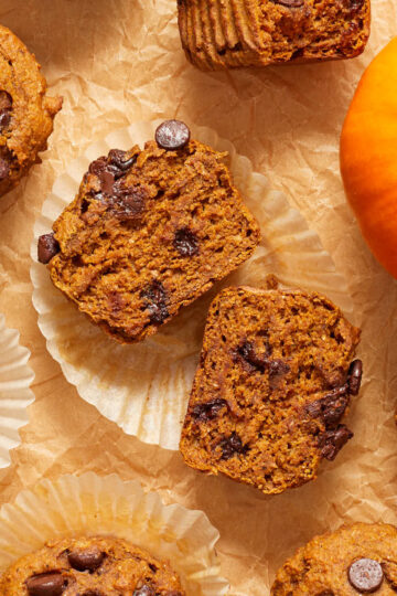 Overhead view of a pumpkin banana muffin cut in half on a paper wrapper.