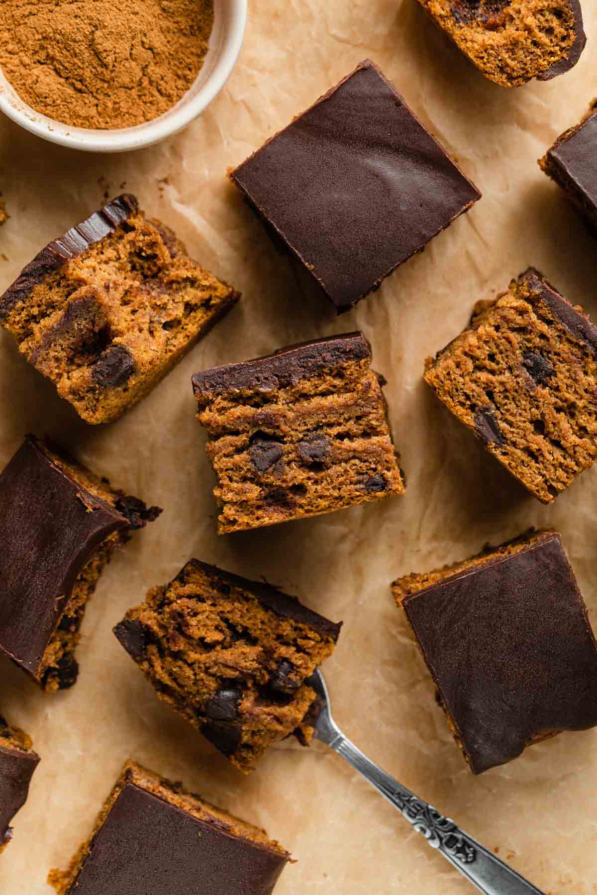 Overhead view of pieces of pumpkin snack cake arranged on a sheet of brown parchment paper.