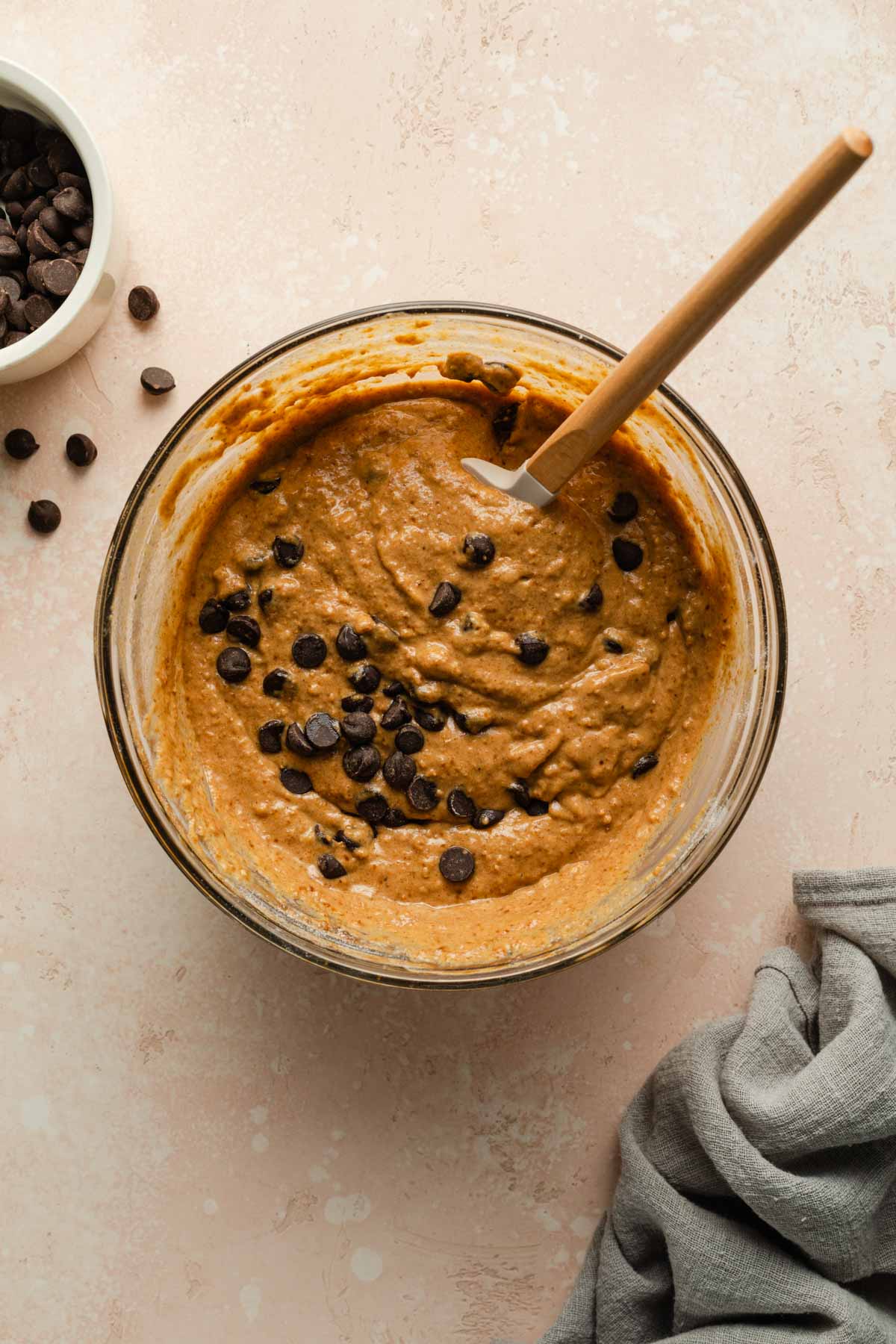 Pumpkin cake batter in a glass bowl topped with chocolate chips and stirred with a spatula.