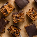 Overhead view of pumpkin snack cake cut into squares and arranged on a sheet of brown parchment paper.