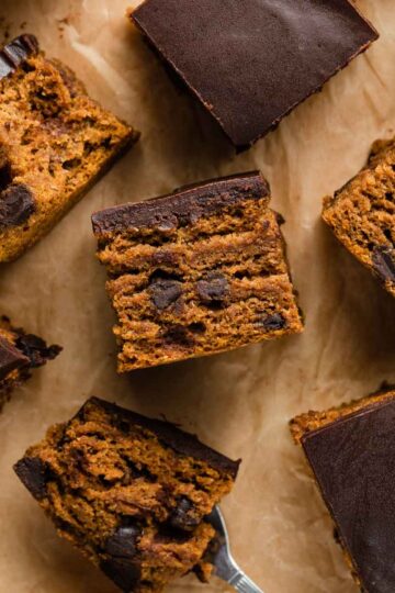 Overhead view of pumpkin snack cake cut into squares and arranged on a sheet of brown parchment paper.