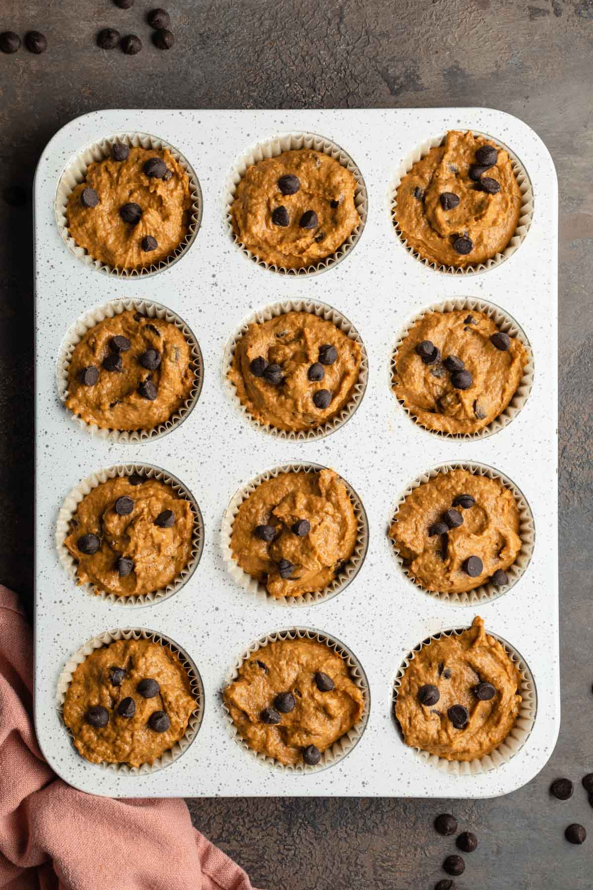 Muffin batter in a muffin pan and topped with chocolate chips.
