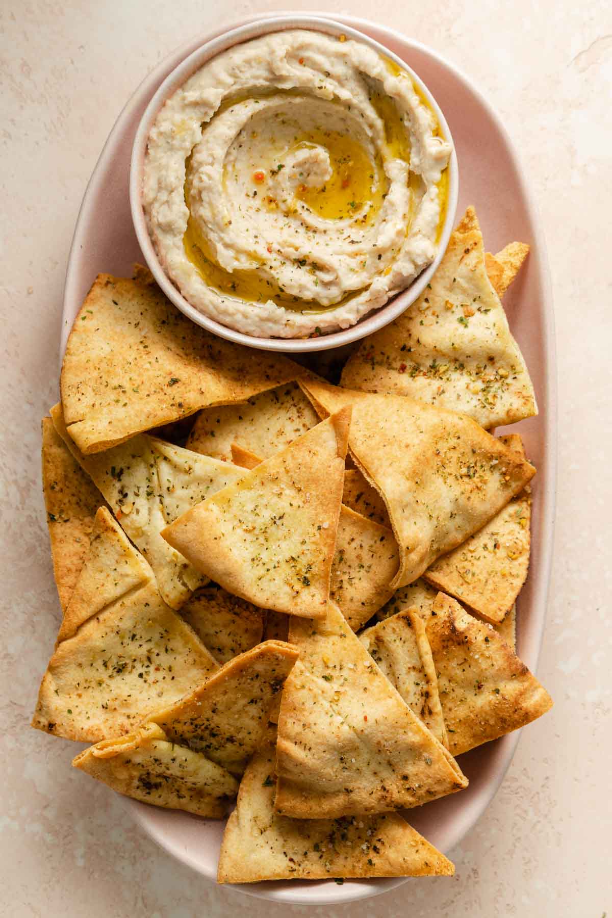 Overhead view of air fried pita chips on a platter with white bean dip.